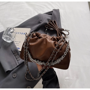 Detail of a brown pleated bucket bag featuring a thick silver chain on grey fabric