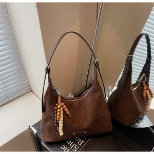 Détail du sac hobo en daim marron foncé avec pompon en perles de bois et boucle métallique
