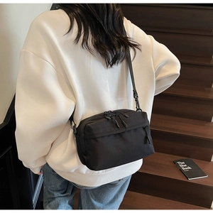 Detail of a black nylon crossbody bag with dual zippers worn over a wooden staircase