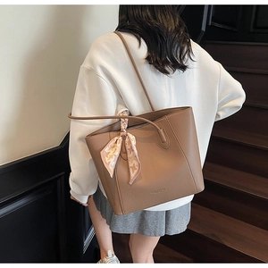 Detail view of brown pebbled leather tote bag featuring an elegant printed silk scarf on handle