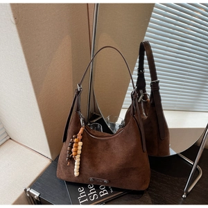 Détail d'un sac à bandoulière en daim marron foncé avec fermeture éclair et breloque en bois