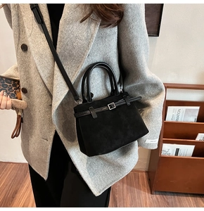 Close-up of a mini black suede tote bag with strap worn with a gray blazer