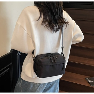 Detail of minimalist black nylon crossbody bag with dual zipper compartments on model