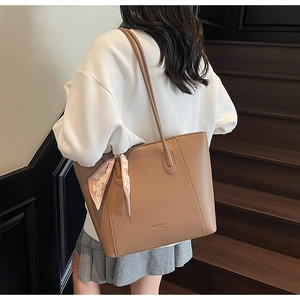 Close-up of a brown tote bag featuring lychee grain leather and decorative silk scarf detail