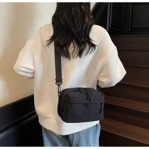 Rear view of a black nylon crossbody bag with adjustable strap shown on a model