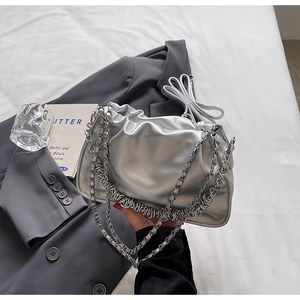 Close-up of silver pleated cloud bag with metallic chain straps on elegant magazine background
