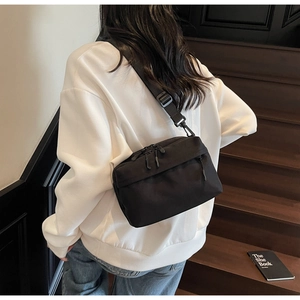 Detail of a black nylon crossbody bag with dual zippers shown on a person on stairs