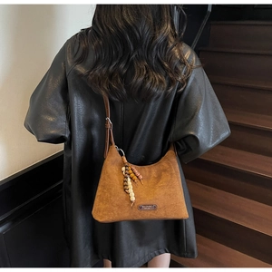 Détail du sac hobo en daim marron avec pompon en perles de bois sur la bandoulière