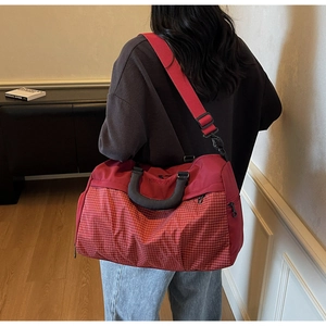 Detail of red checkered travel bag featuring a reinforced handle and adjustable shoulder strap
