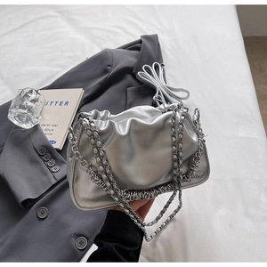 Detail of silver metallic pleated cloud bag with stylish chain straps on grey blazer