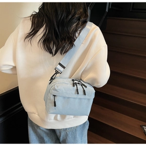 Detail of light blue nylon crossbody bag featuring three zipper pockets and wide strap