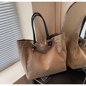 Detail view of large khaki tote bag with knot decor handles reflected in a mirror