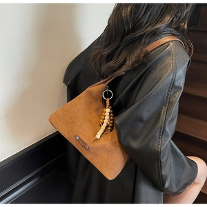 Gros plan sac en daim marron avec pendentif perles en bois vintage et plaque de marque métal