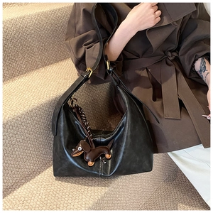 Detail of glossy black leather shoulder bag with cute dachshund charm and gold buckle