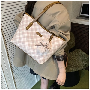 Detail view of large plaid tote bag with brown leather handles and plush bunny charm