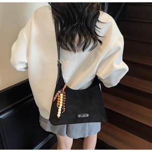 Détail du sac en daim noir avec pompon en perles colorées et plaque de logo