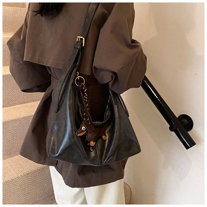 Detail of black leather dumpling bag with cute dog charm and golden hardware strap