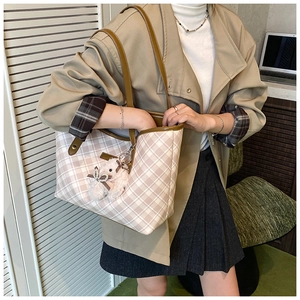 Detail of beige plaid tote bag featuring brown leather straps and a plush bear charm