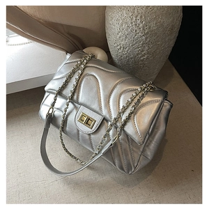 Close-up of silver quilted crossbody bag with gold rectangular turn-lock and chain strap