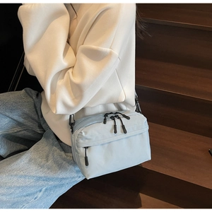 Close-up of a light blue nylon crossbody bag with black zippers on a lifestyle background