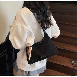 Détail du sac sous le bras en daim noir avec pendentif en perles et logo métallique
