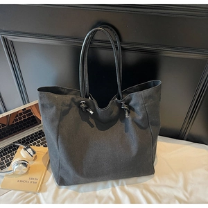 Detail of black canvas tote bag showing drawstring knots and metal rivet accents