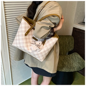Detail of checkered tote bag featuring leather trim and a plush rabbit charm accessory