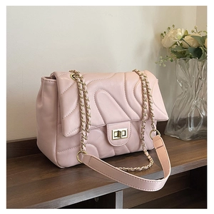 Detailed view of pale pink quilted shoulder bag with golden chain and wave stitching