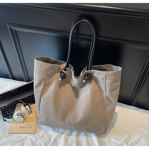 Detail of taupe tote bag featuring knotted black handles and silver metallic hardware accents