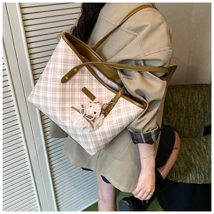 Detail of pink plaid tote bag with brown leather straps and a plush rabbit charm