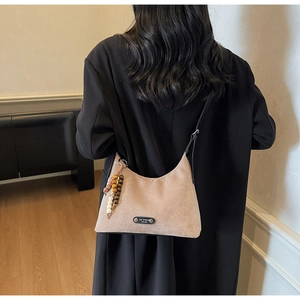 Détail du sac hobo en daim kaki avec pompon en perles et plaque logo porté par mannequin