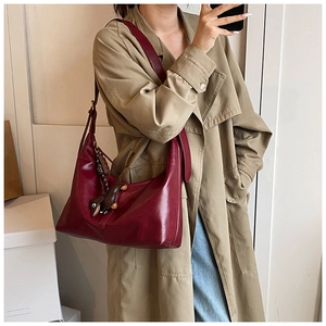 Detail of dark red hobo bag with sleek finish and decorative dog charm accessory