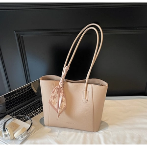 Detailed shot of beige leather tote bag with silk scarf, laptop, and workplace items