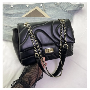 Close-up of black quilted chain bag with gold rotary lock on white fabric background