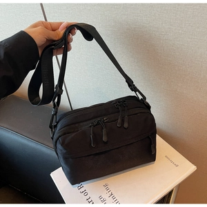 Detail of black crossbody bag featuring multiple zipper compartments and wide strap