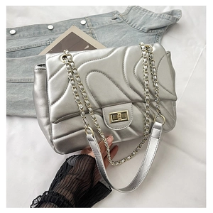 Close-up of silver quilted crossbody bag with golden chain strap and wave stitching detail