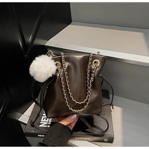 Détail du sac seau à cordon marron foncé avec chaîne dorée et breloque boule en peluche