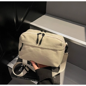 Detail of light beige nylon crossbody bag with multi-layer zippers on black books