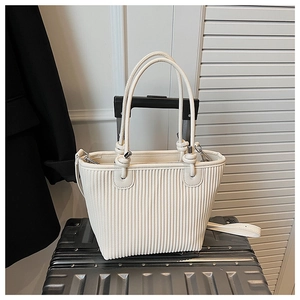 Detail of cream pleated tote bag with knot handle placed on luggage for travel