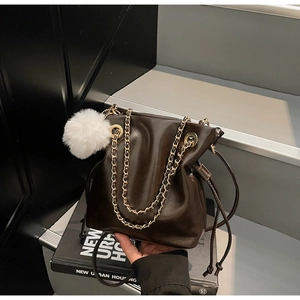 Détail du sac seau marron foncé à cordon avec chaîne dorée et pompon blanc
