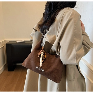 Détail du sac à bandoulière en daim marron foncé avec pompons en perles de bois