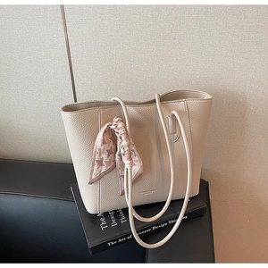 Close-up of beige lychee leather tote bag with stylish houndstooth silk scarf on a book