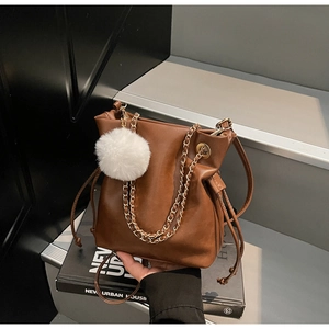 Détail d'un sac seau en cuir marron avec chaîne dorée et pompon en peluche blanche