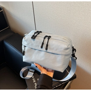 Detail showing a light blue nylon crossbody bag with black dual-zippers and wide strap