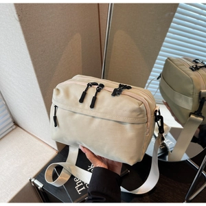 Detail of a beige nylon crossbody bag with multi-zipper compartments and wide woven strap