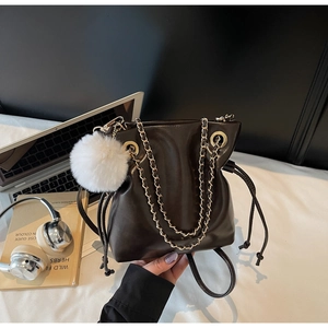 Détail du sac seau marron foncé en simili cuir avec chaîne dorée et pompon décoratif