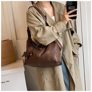 Detail shot of a dark brown retro hobo bag with bow charm on a trench coat model