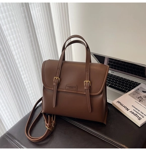 Brown faux leather briefcase bag with top handles and adjustable strap on a desk