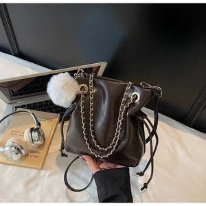 Détail du sac seau marron café avec chaîne dorée et breloque peluche dans un cadre maison