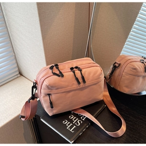 Detail view of pink nylon crossbody bag with multiple zippers on black book